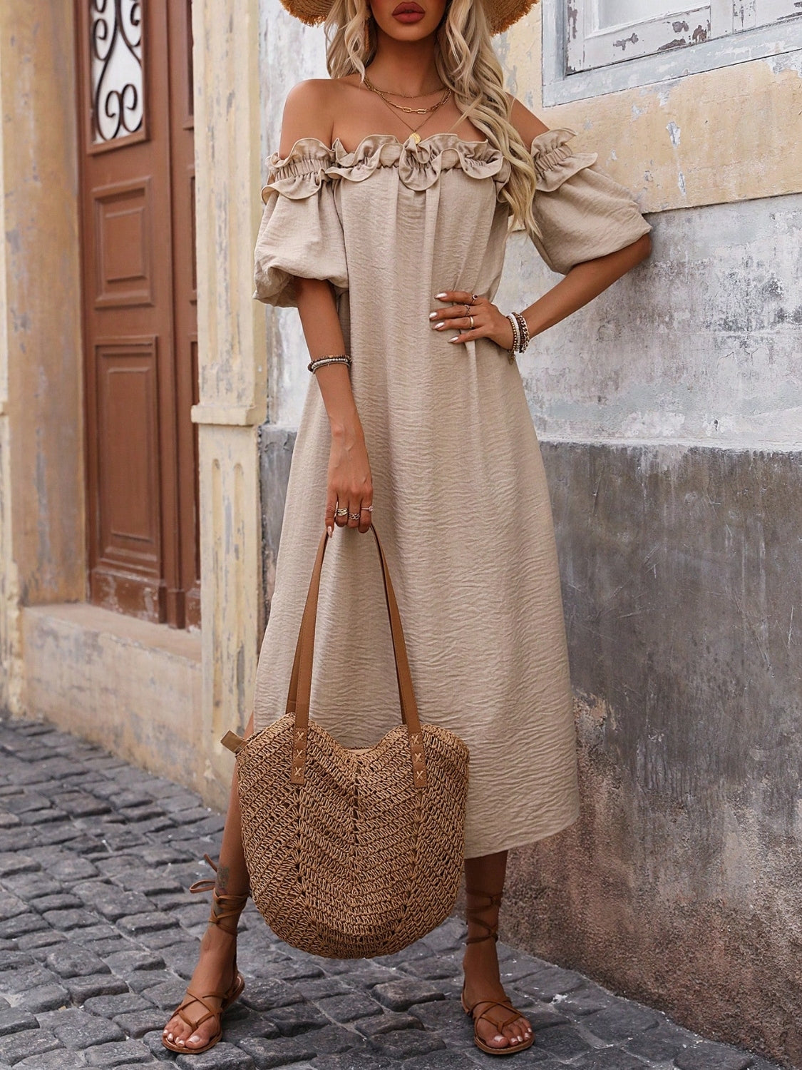 Women's tan off-shoulder midi dress with ruffled neckline and puff sleeves, styled on model wearing a straw hat.