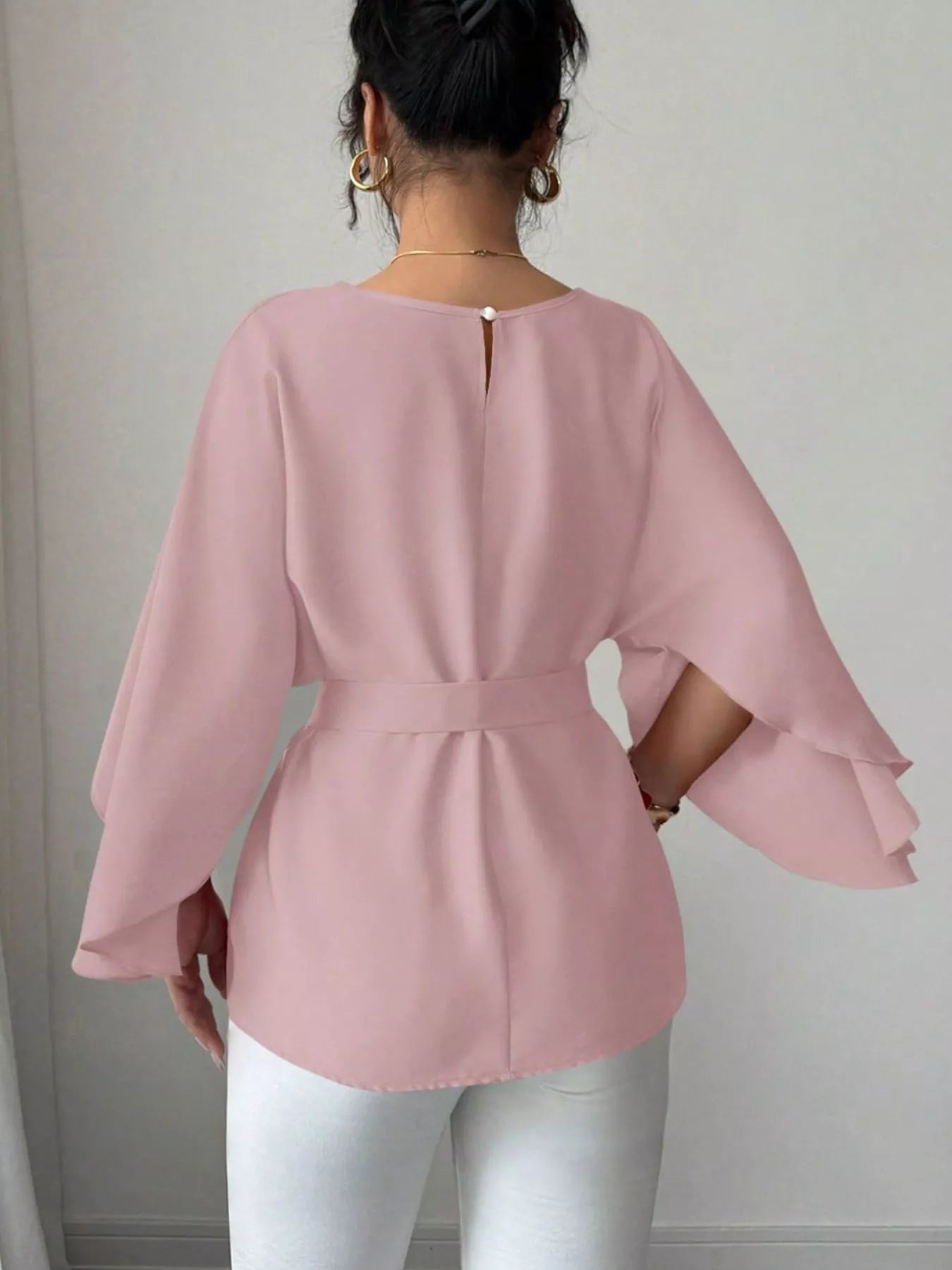 Back view of pink batwing sleeve blouse showing button keyhole neckline and belted waist