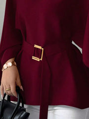 Close detail of burgundy batwing sleeve blouse gold buckle belt and flared hem