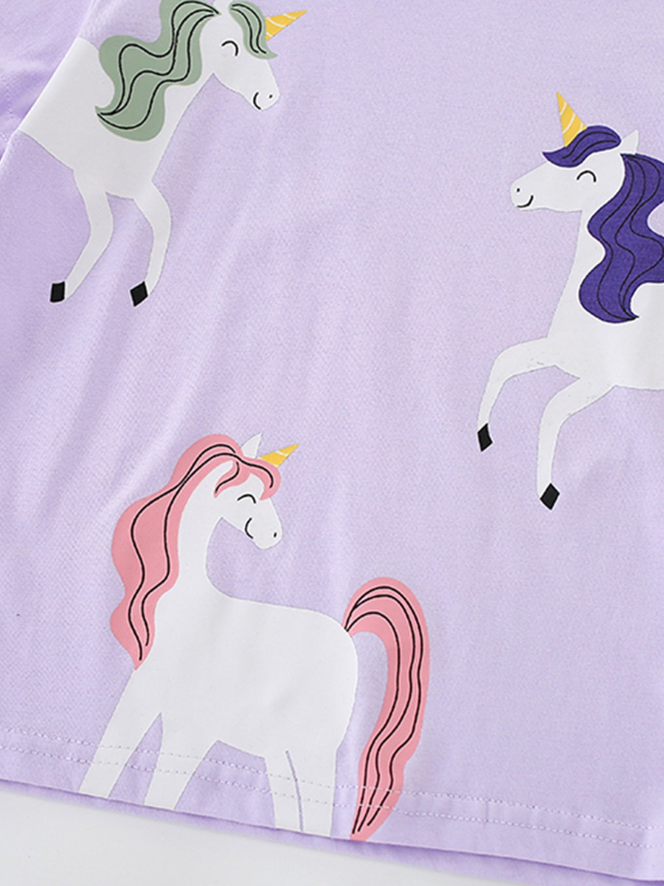 Close view of the three white unicorn graphics with colorful manes on the light purple T-shirt