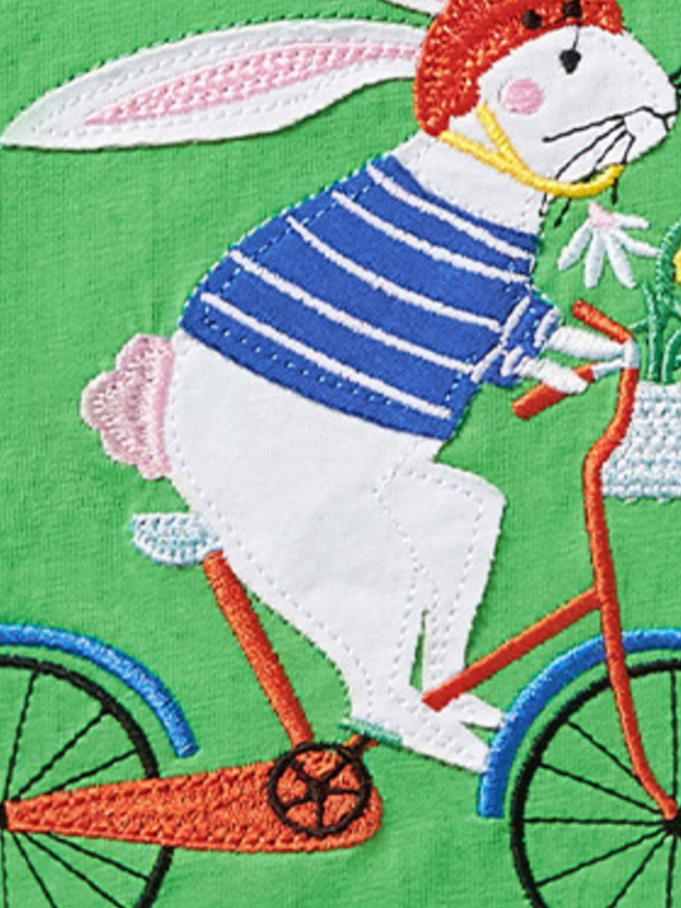 Close view of the embroidered rabbit in a striped top and red helmet riding a bicycle
