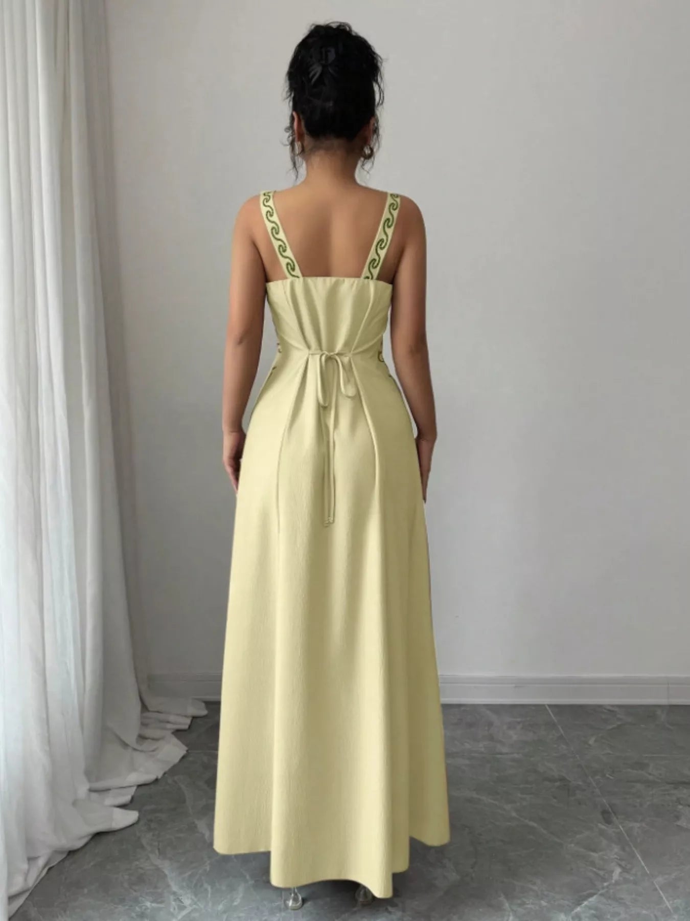 Back view of pastel yellow sleeveless maxi dress with tied waist and patterned straps