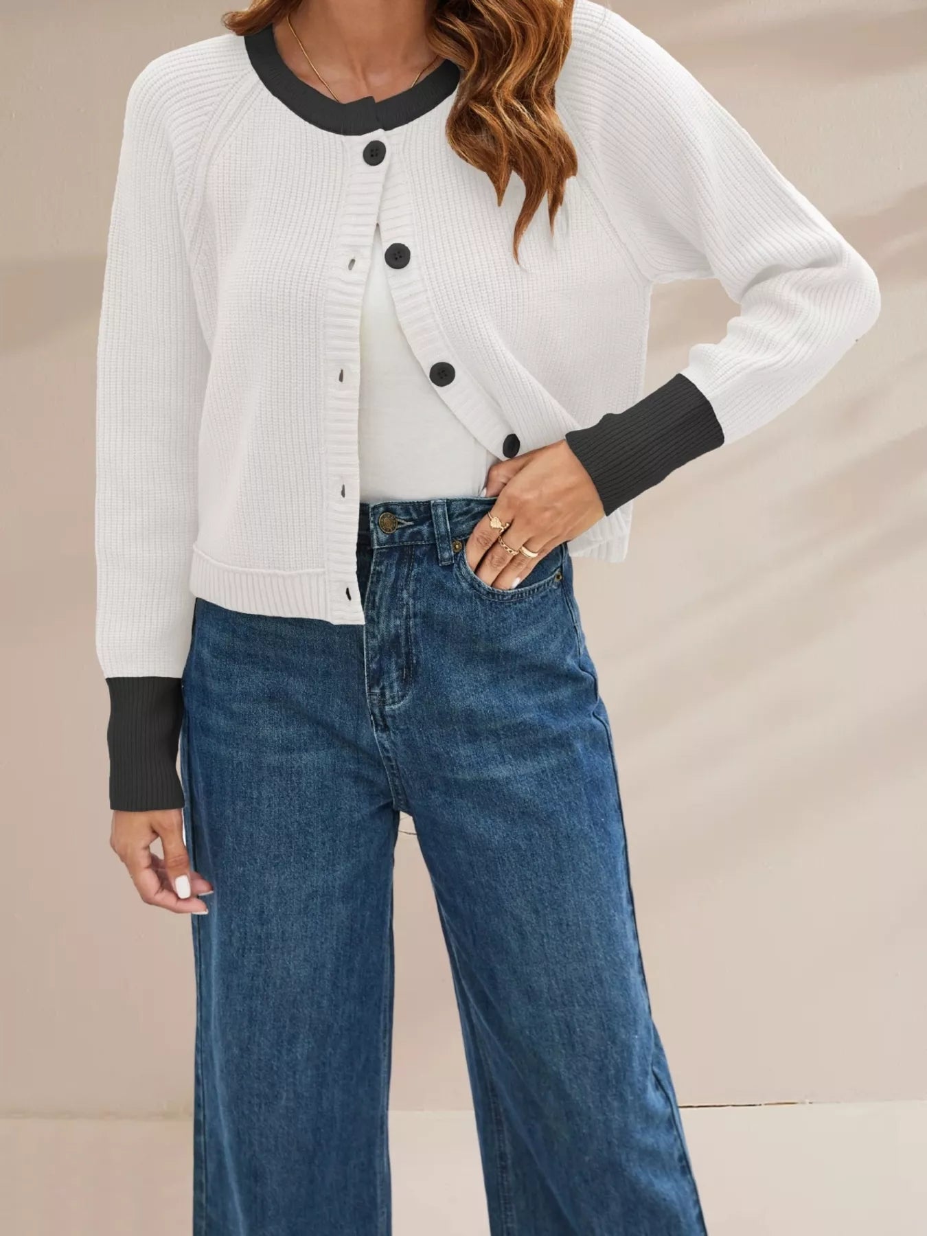 On-model front view of a white ribbed cardigan with black trim and black buttons