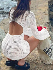 Back view of white crochet dress with large back cutout, model crouching by shore