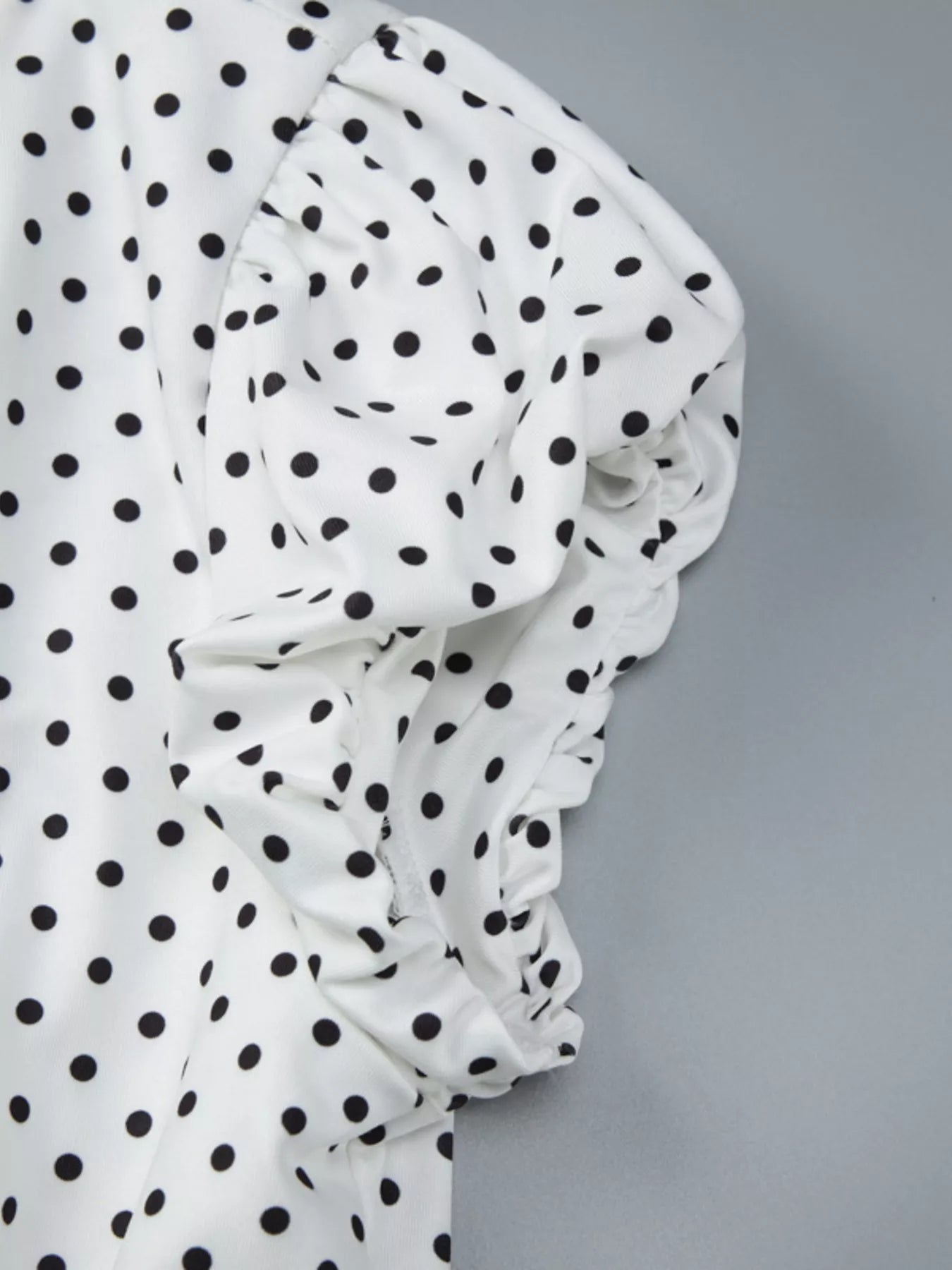 Close-up detail of white fabric with black polka dots and ruched folds from the V-neck top