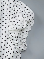 Close-up detail of white fabric with black polka dots and ruched folds from the V-neck top
