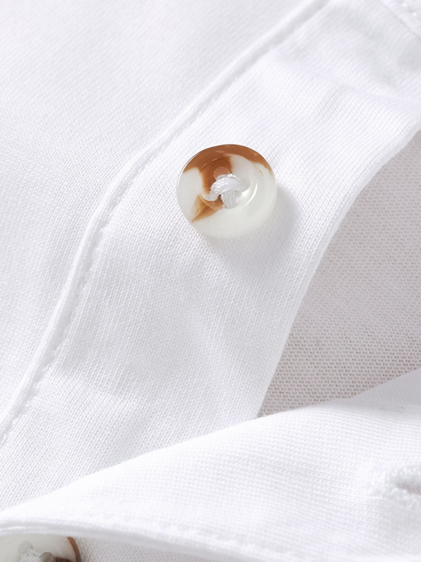 Close detail of a mottled button on the placket of a white children's polo shirt