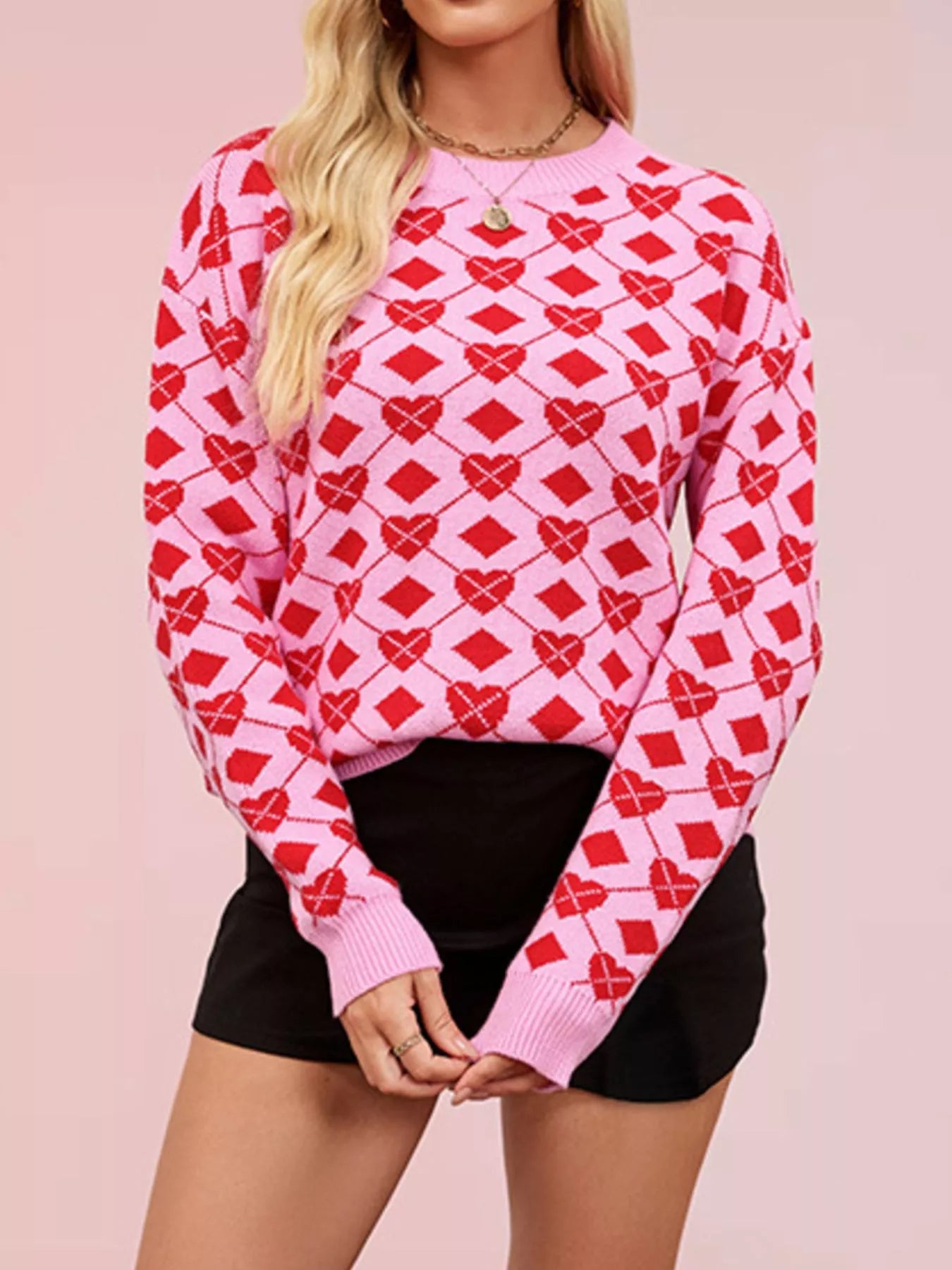 On-model front view of a pink knit sweater with red heart and diamond argyle pattern