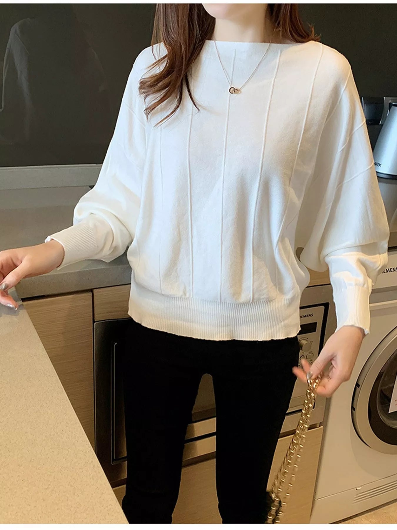 Front view of a white batwing sleeve knit top with vertical seams, worn indoors.