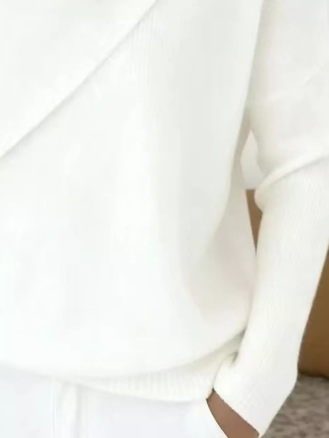 Close-up of the white sweater lower body and long sleeve showing the ribbed hem and knit texture