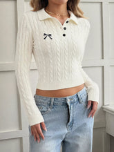 White cable knit long sleeve sweater with polo collar, black buttons and small bow embroidery