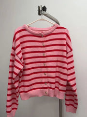 Pink and red striped button down cardigan hanging on a hanger against a plain wall