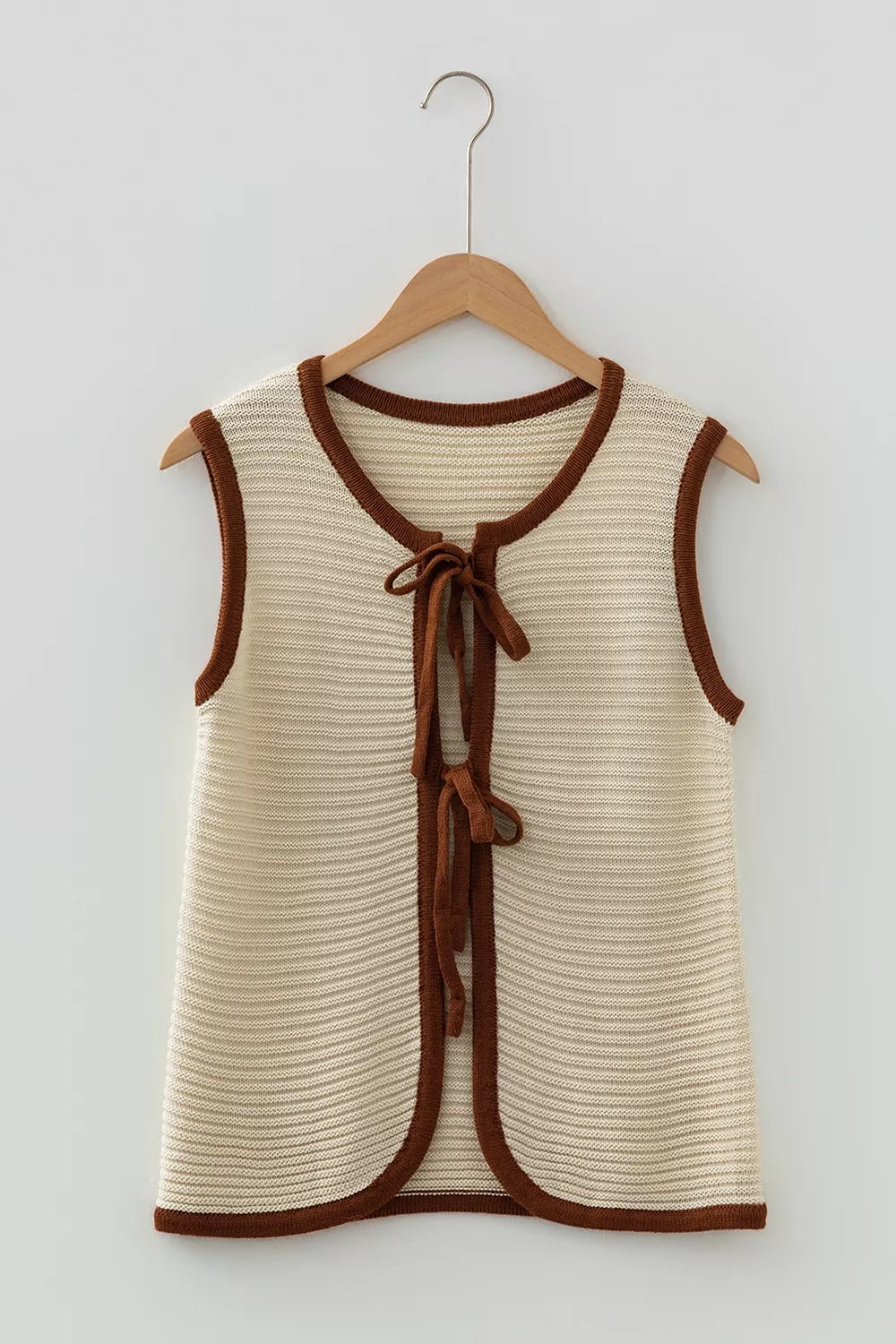 Flat lay front view of a beige tie front sweater vest with brown contrast trim on hanger