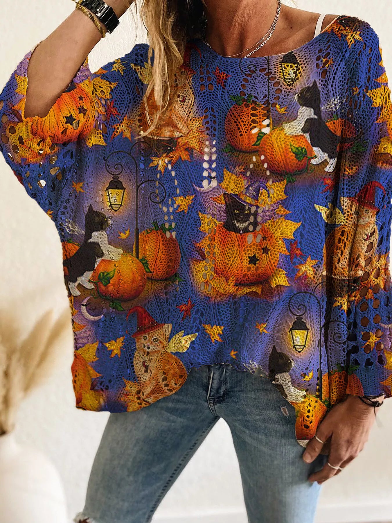 Front view of a blue openwork knit cover up with cats, pumpkins, lanterns, and autumn leaves.