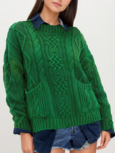 Front view of green cable knit sweater with front pockets layered over denim and shorts