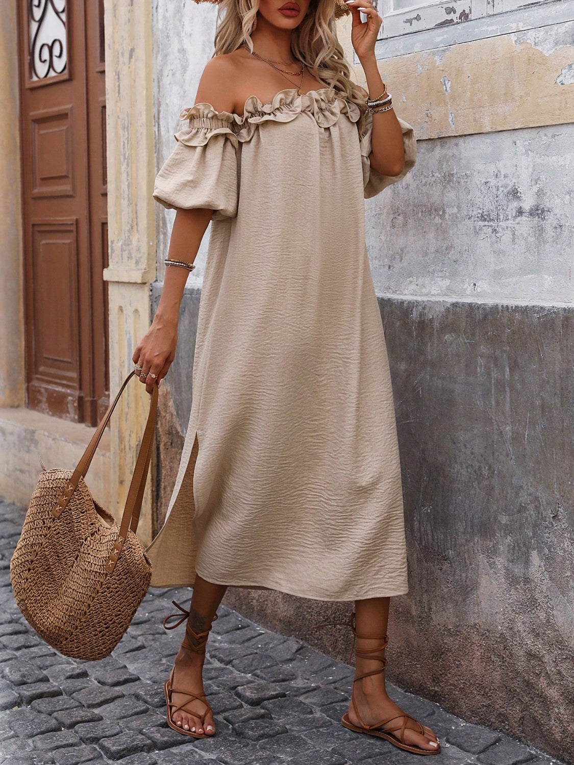 Three-quarter view of women's tan off-shoulder midi dress with ruffled trim, puff sleeves, and woven bag.
