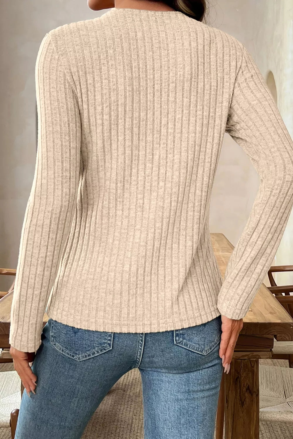 Back view of a beige ribbed long-sleeve cowl-neck top worn with blue jeans