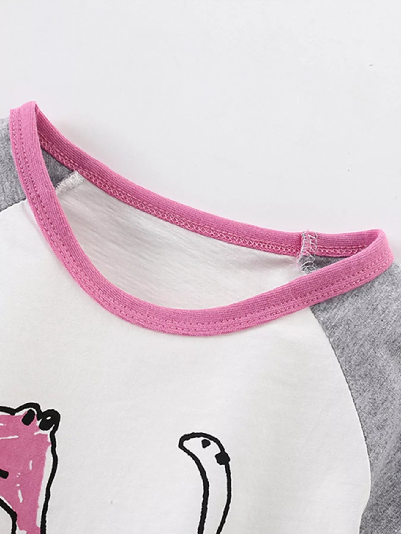 Close-up of the pink crew neckline and gray raglan sleeve on the white children's shirt