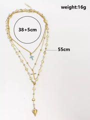 Flat lay of layered gold necklaces with length measurements, blue cross and heart pendant