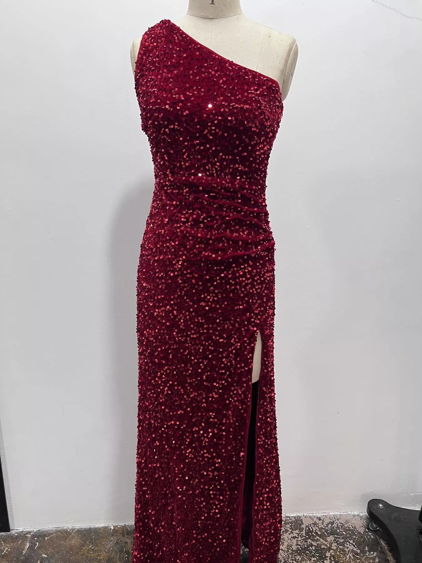 Burgundy sequin one shoulder evening dress shown front facing on a dress form with a high slit