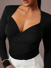 Close cropped front view of black ruched surplice bodysuit paired with white trousers