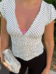 White polka dot ruched V-neck top with short sleeves, button front, and visible pink camisole underneath