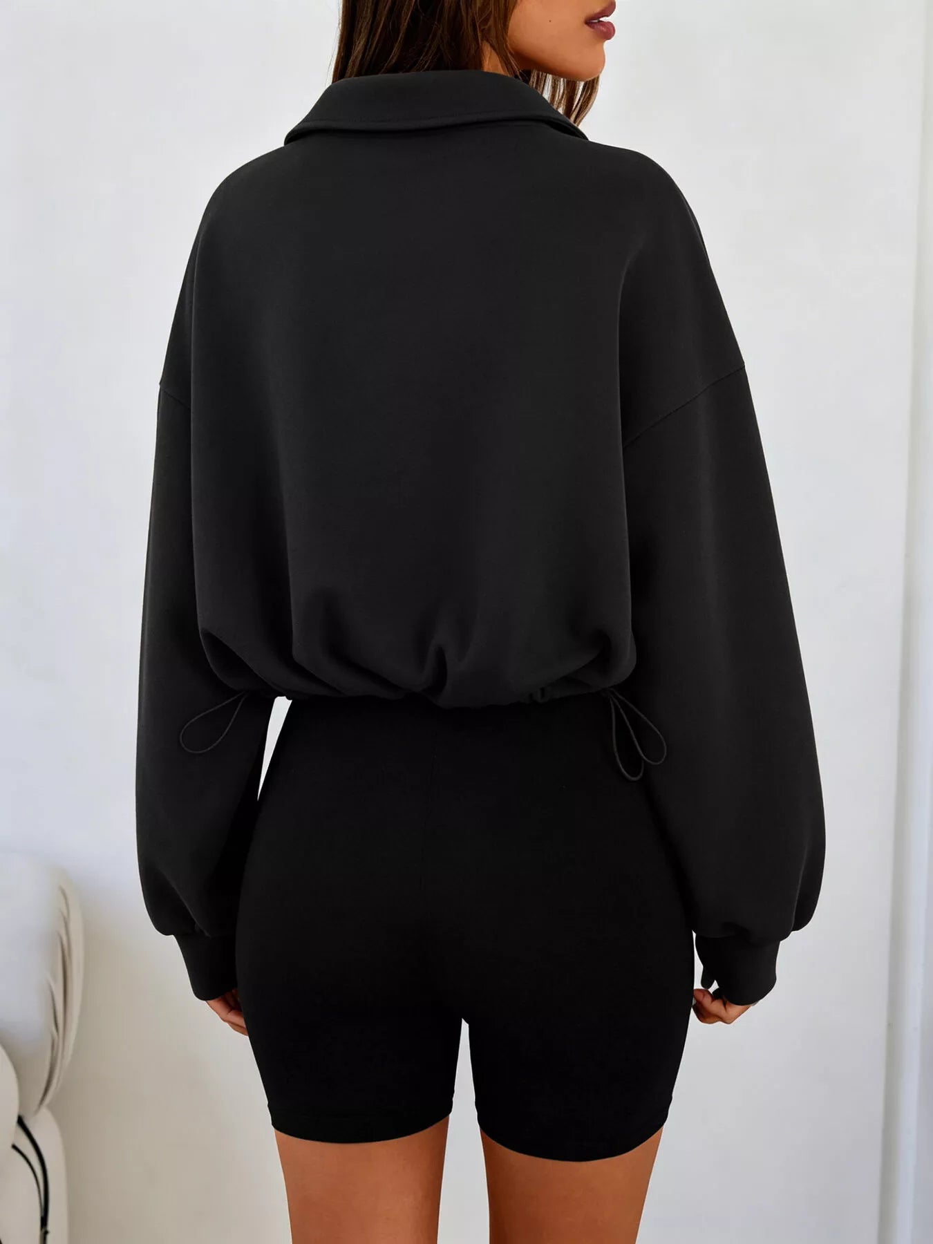 Back view of black half zip sweatshirt with drawstring hem and relaxed fit