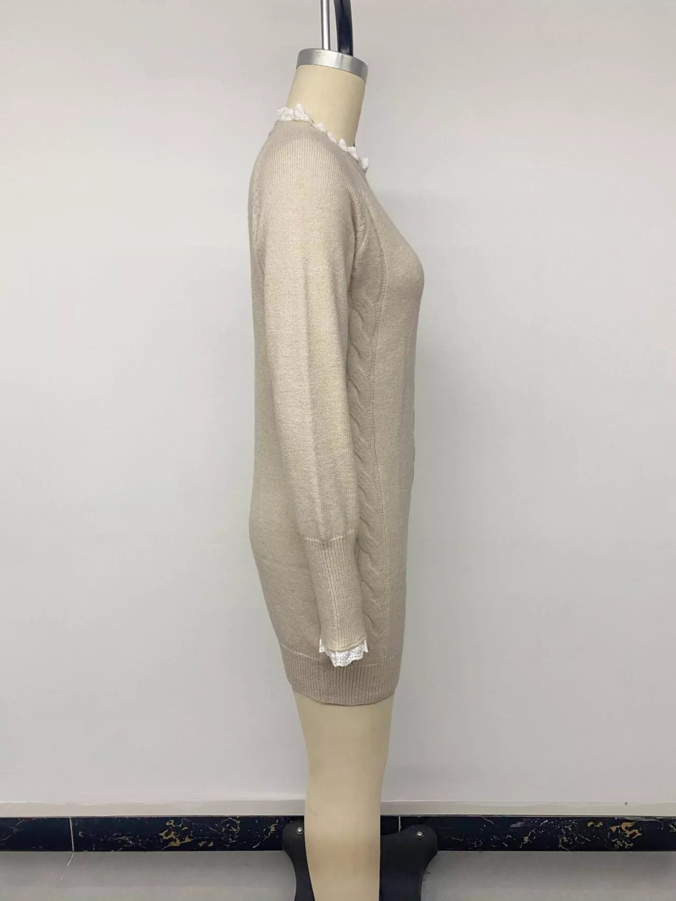 Side view of beige cable knit sweater dress on a mannequin showing lace cuffs and ribbed hem