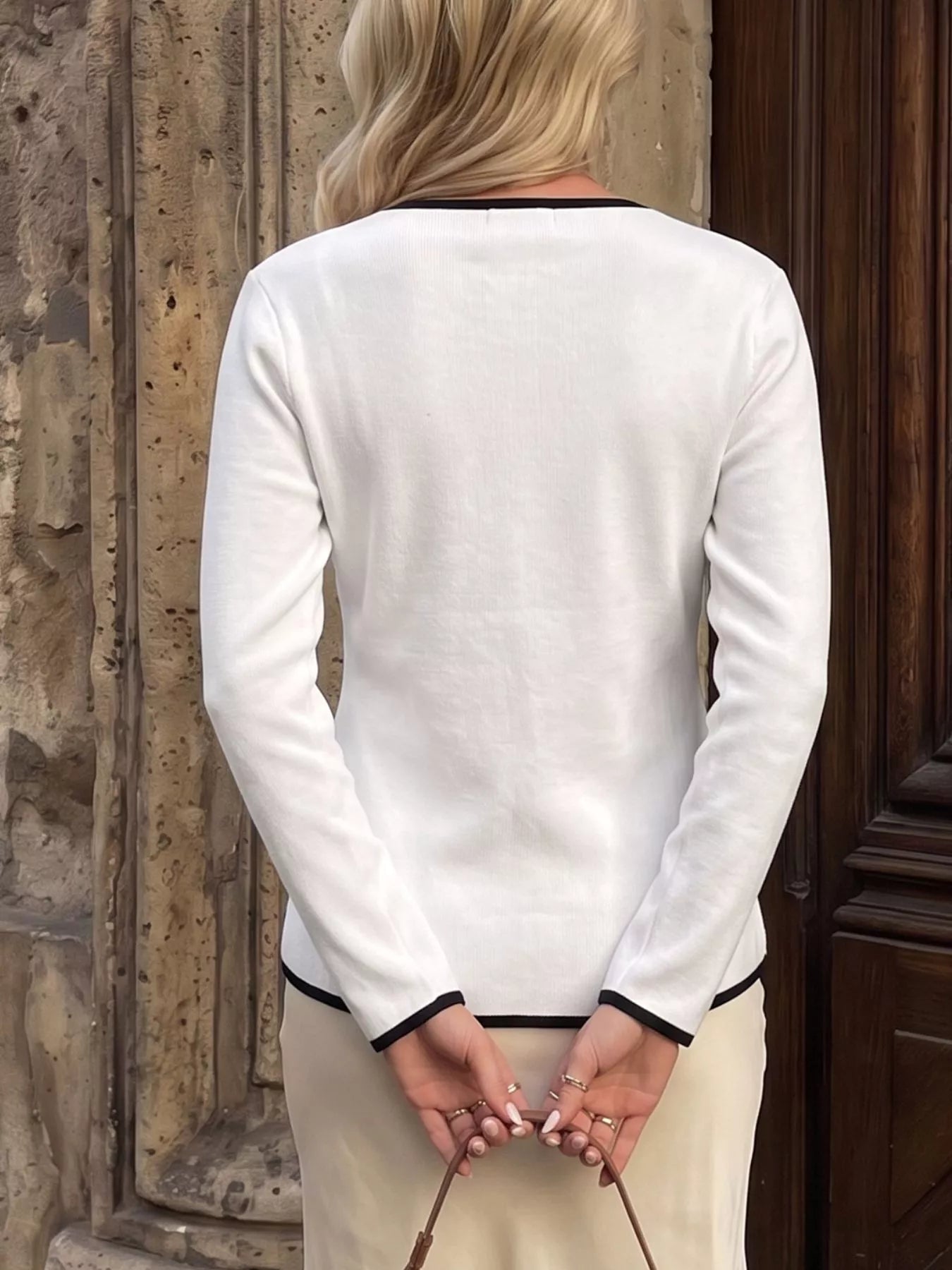 Back view of white long sleeve knit top with black trim at neckline and cuffs.