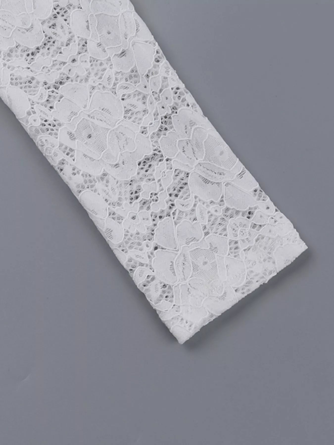 Flat detail of a white lace maxi dress sleeve showing the floral lace pattern