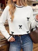 Front view of a white long sleeve sweater with black bows and lace trim at the collar and cuffs