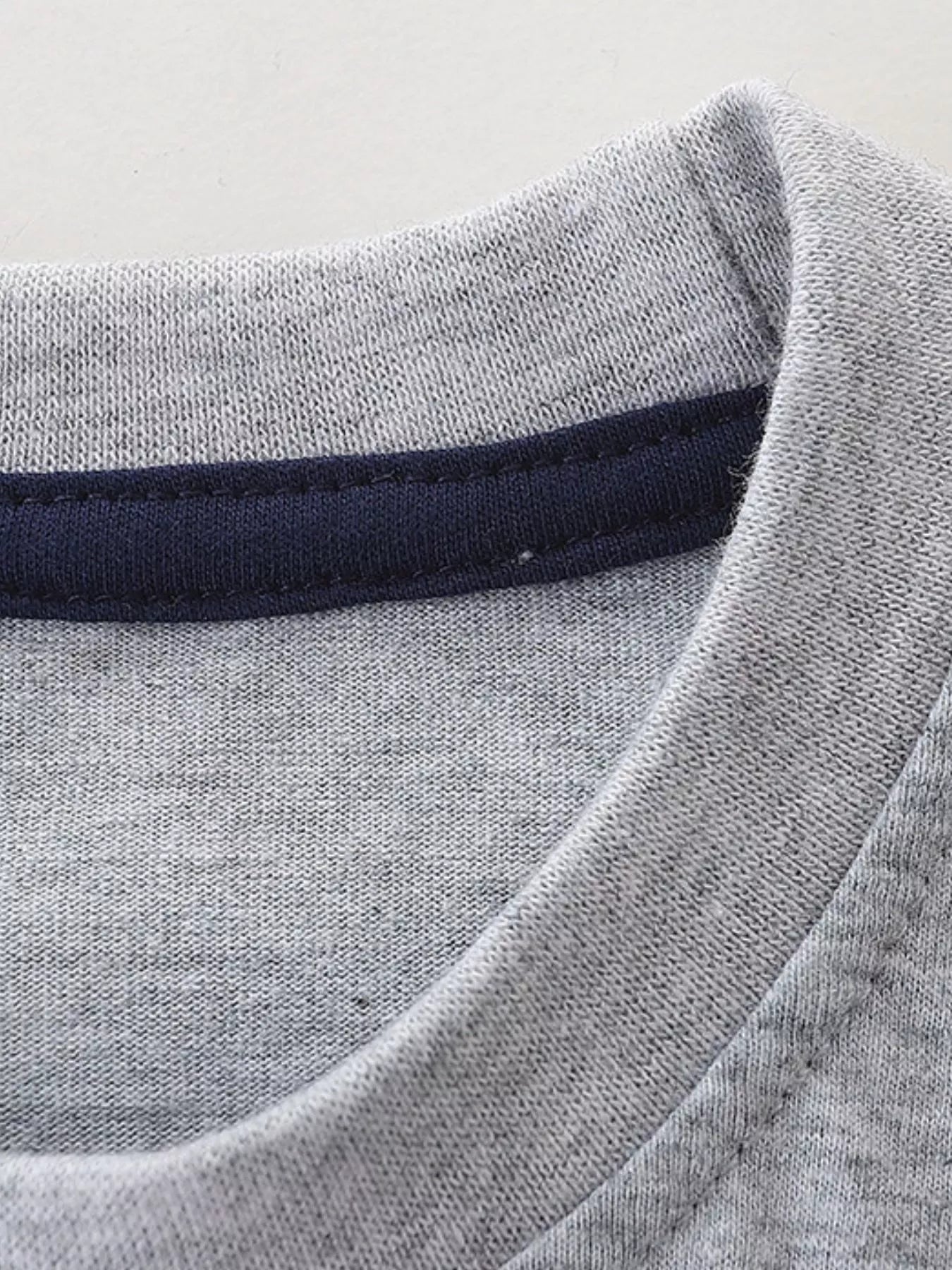 Close-up of light gray children's t-shirt neckline with dark navy inner trim and stitching