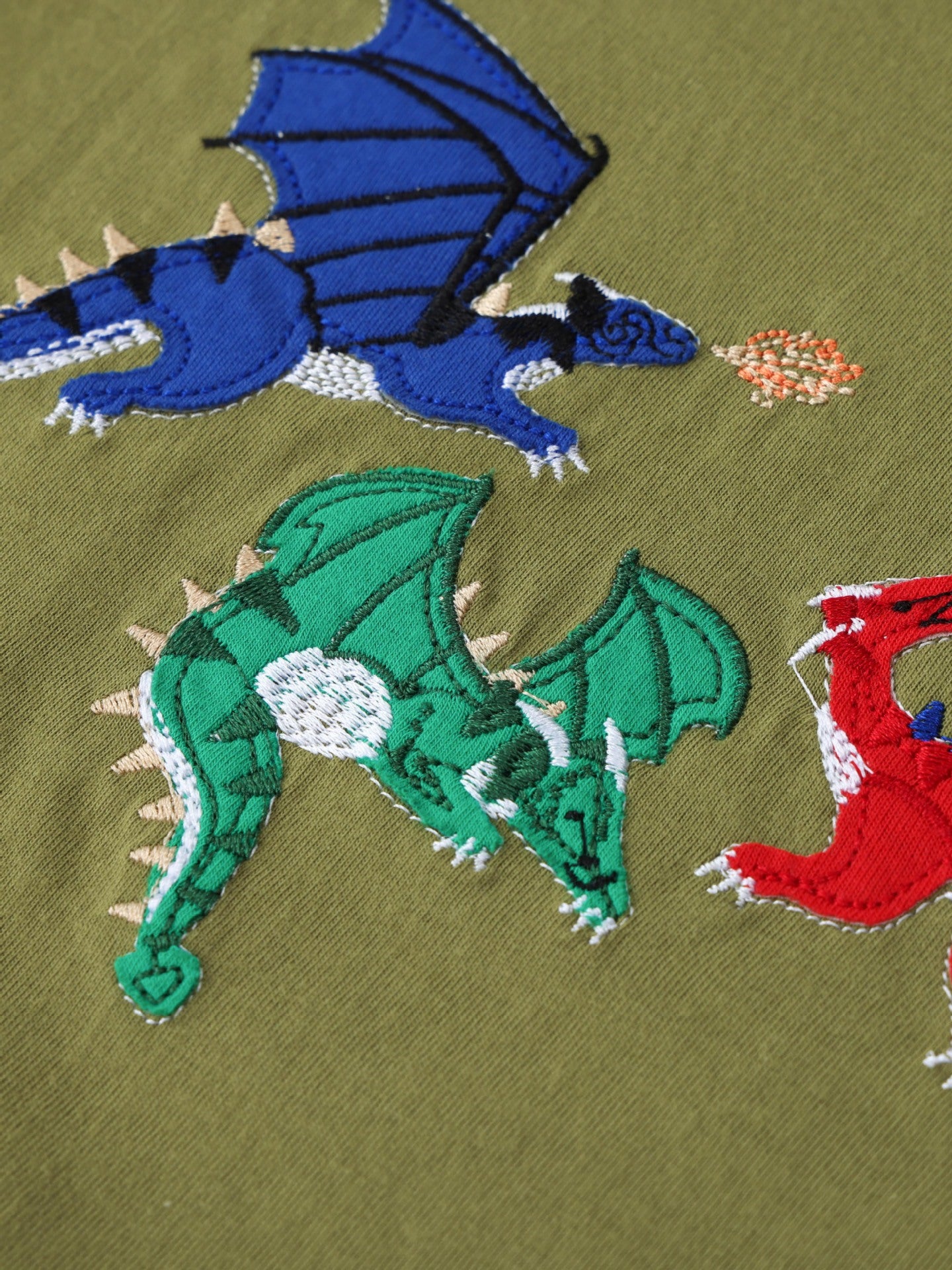 Close-up of embroidered blue and green dragons with detailed stitching on olive t-shirt