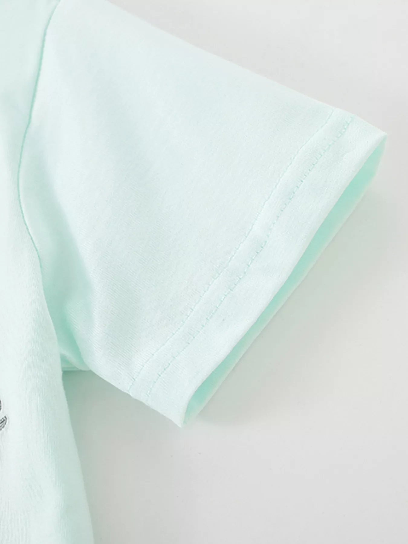 Close-up of the mint blue short sleeve hem with fine stitching on a children's polo shirt