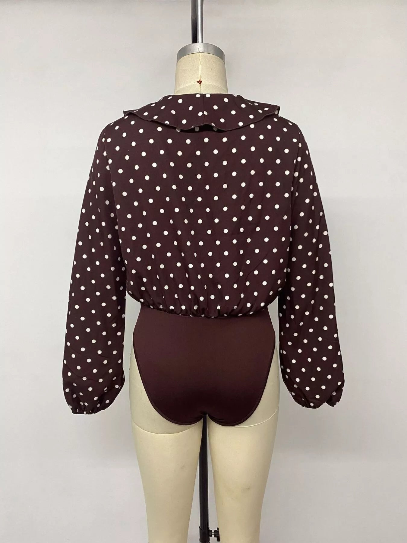 Mannequin back view of a coffee brown polka dot bodysuit with long sleeves