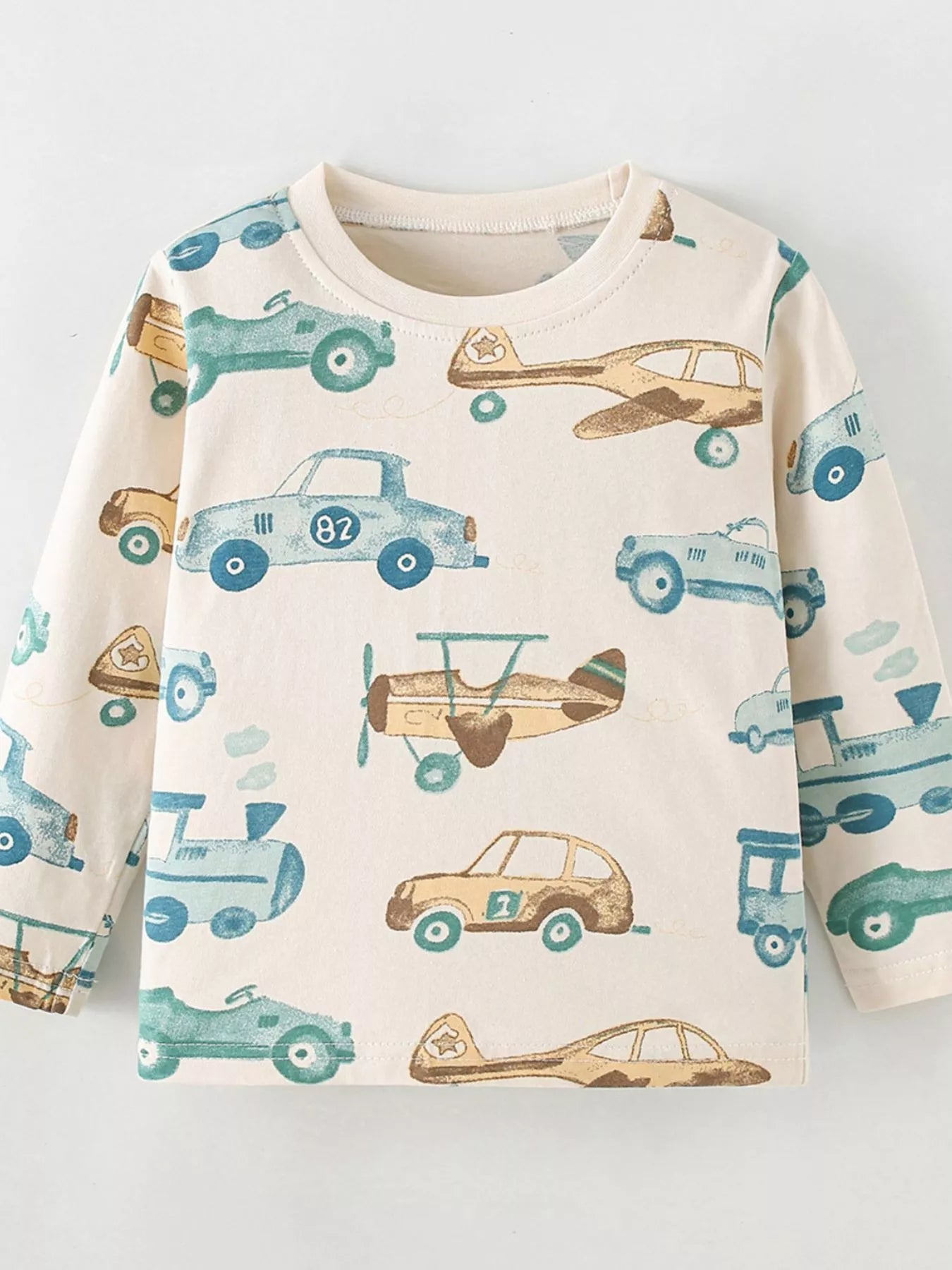 Cream children's long sleeve T-shirt laid flat with a blue and tan cars, planes and trains print