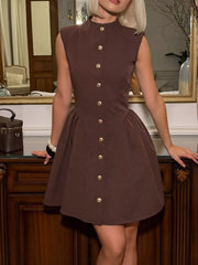 Brown sleeveless button down mini dress with gold buttons, model leaning on cabinet
