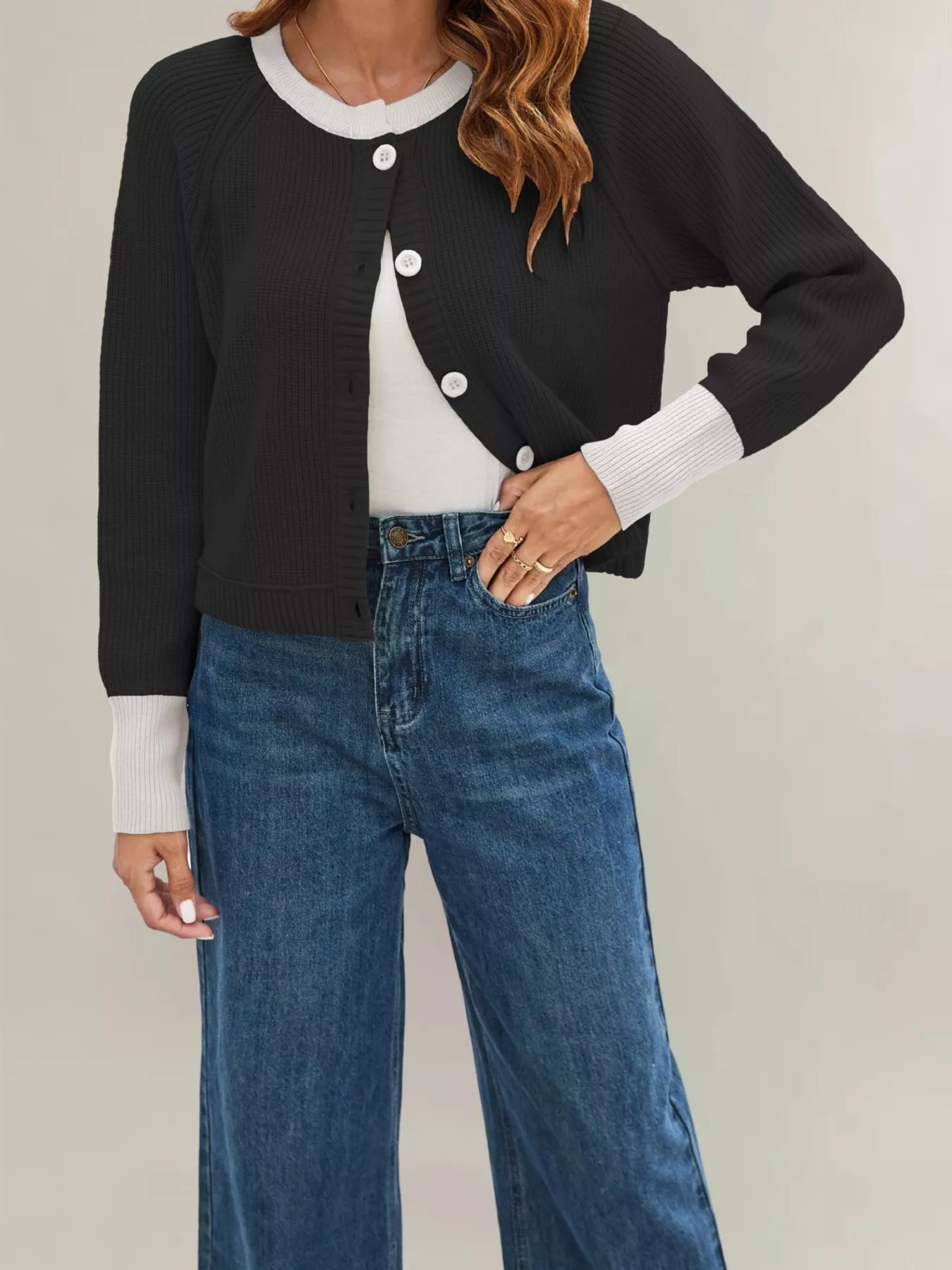 On-model front view of a black ribbed cardigan with cream trim and white buttons