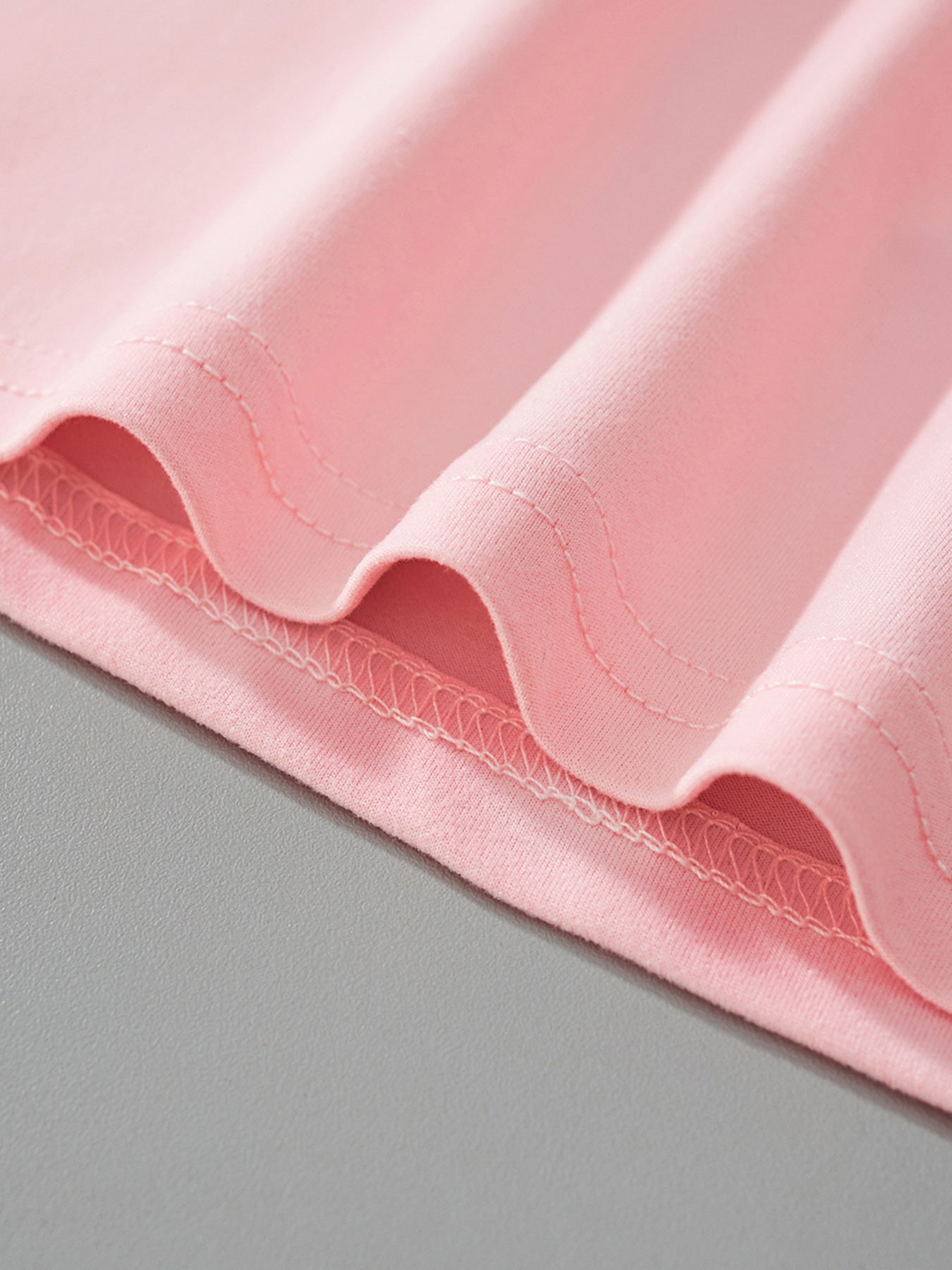 Close-up of the blush pink fabric and stitching at the hem of the children's t-shirt