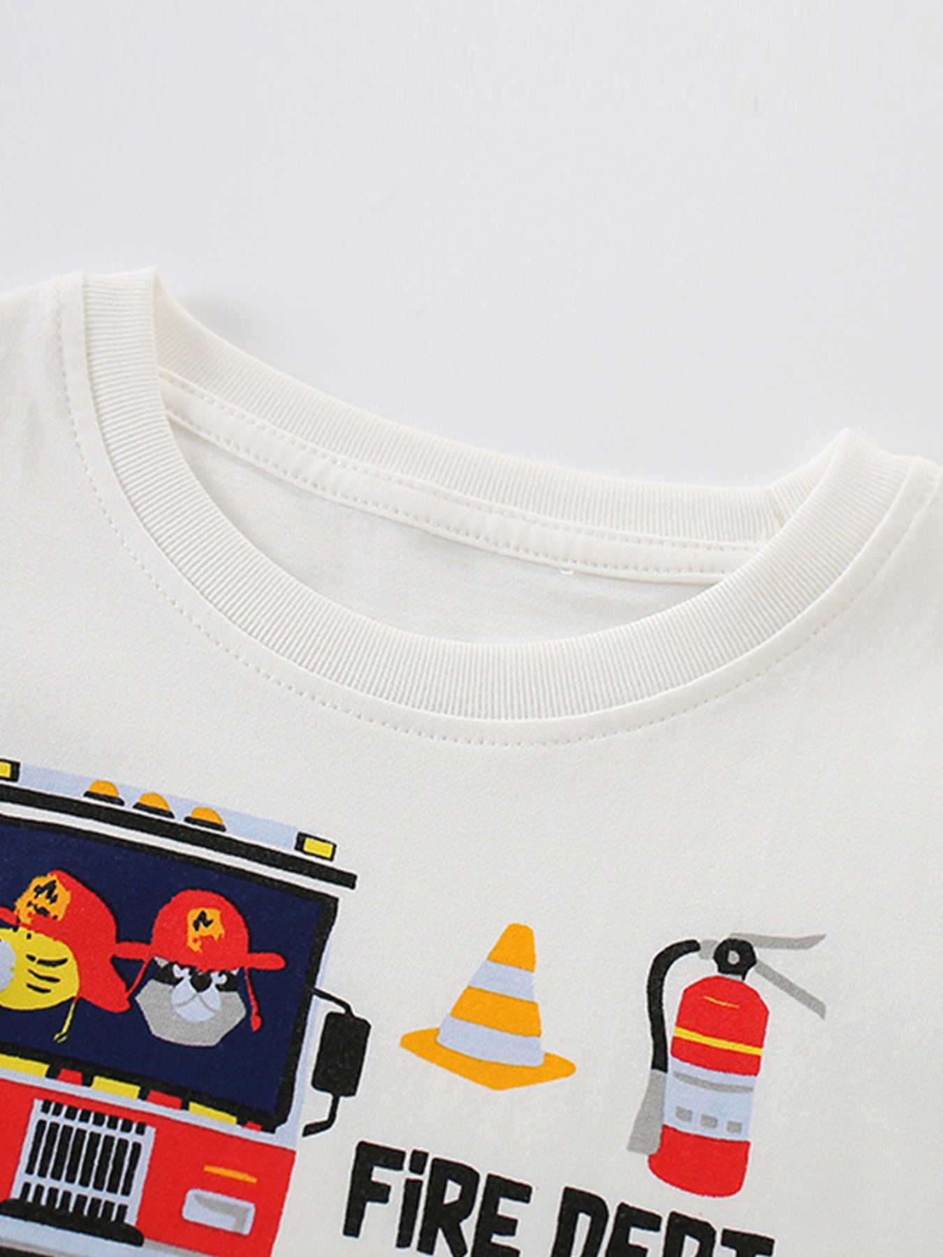 Angled close-up of white children's t-shirt collar with fire truck cone and extinguisher