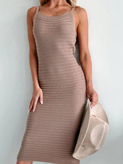 Front view of camel sleeveless knit bodycon sweater dress holding a hat against a wall
