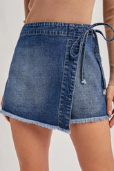 Women's wrap-front denim skort with a tied waist and raw hems.
