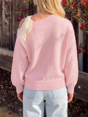 Back view of a plain pink one-shoulder sweater with a cream bow at the shoulder
