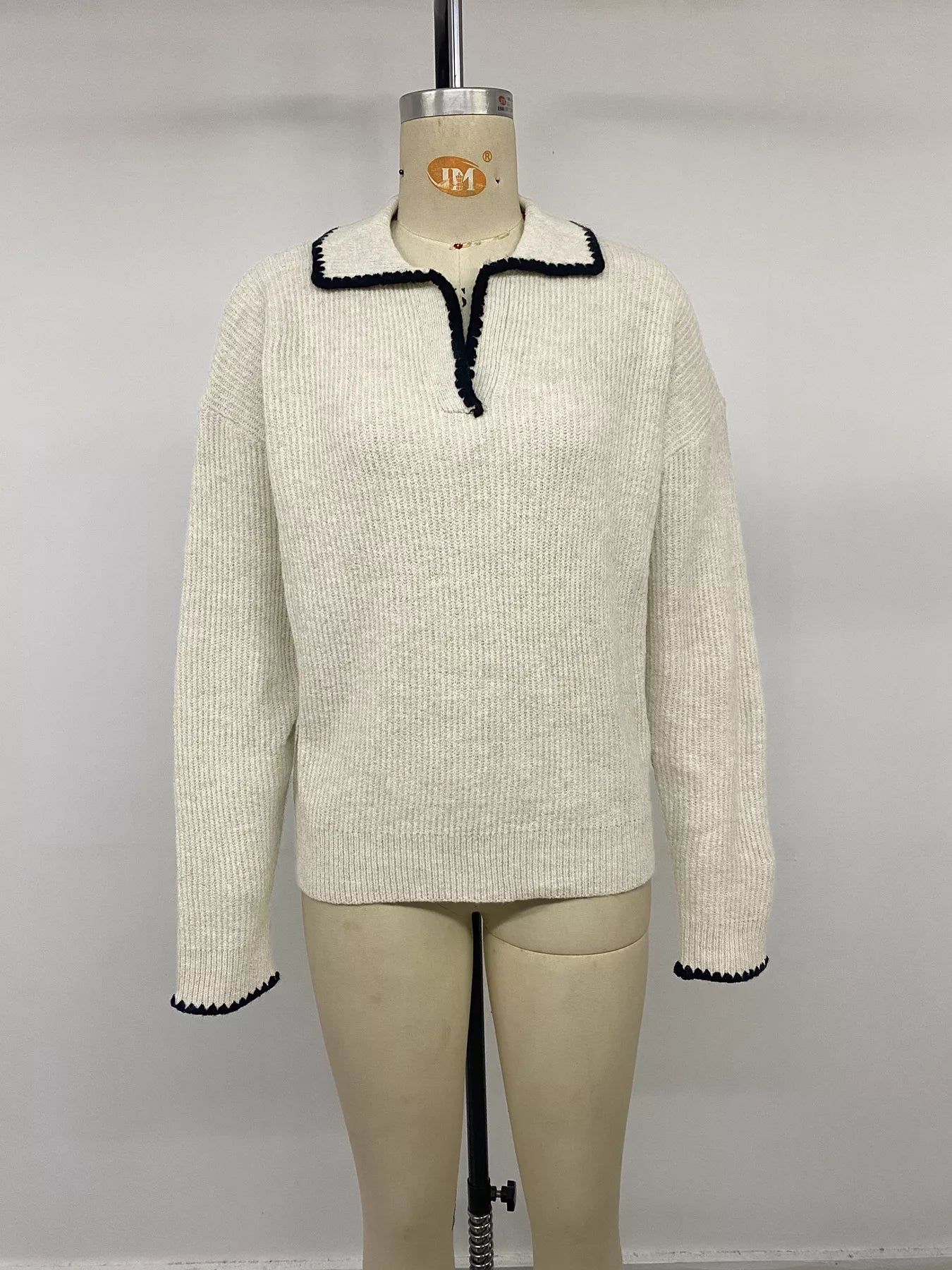 Front view on a mannequin of a cream ribbed sweater with black scalloped collar trim