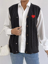 Black cable knit V neck vest open over white shirt with red heart