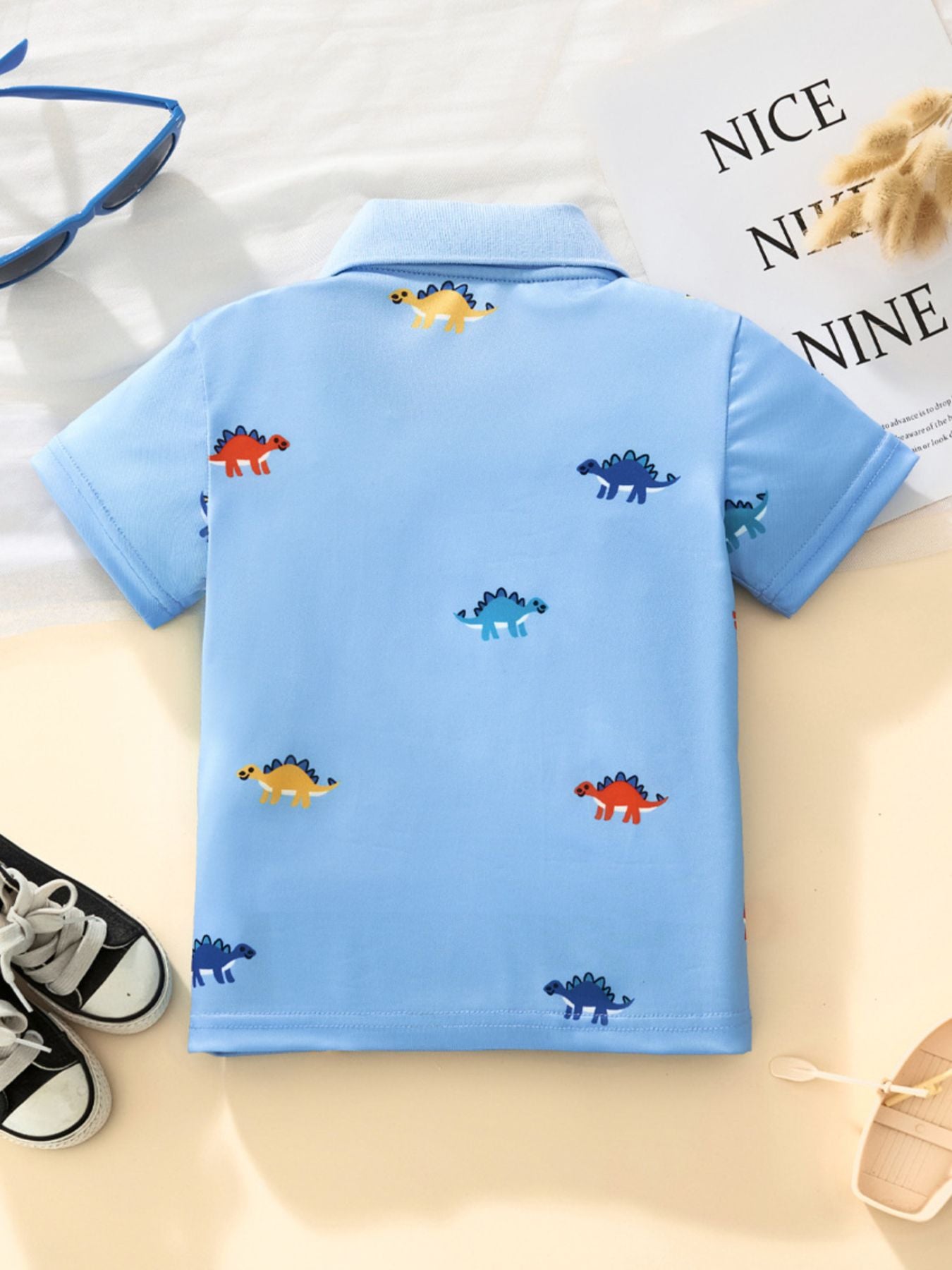 Back view of a sky blue children's polo shirt with small colorful dinosaur prints