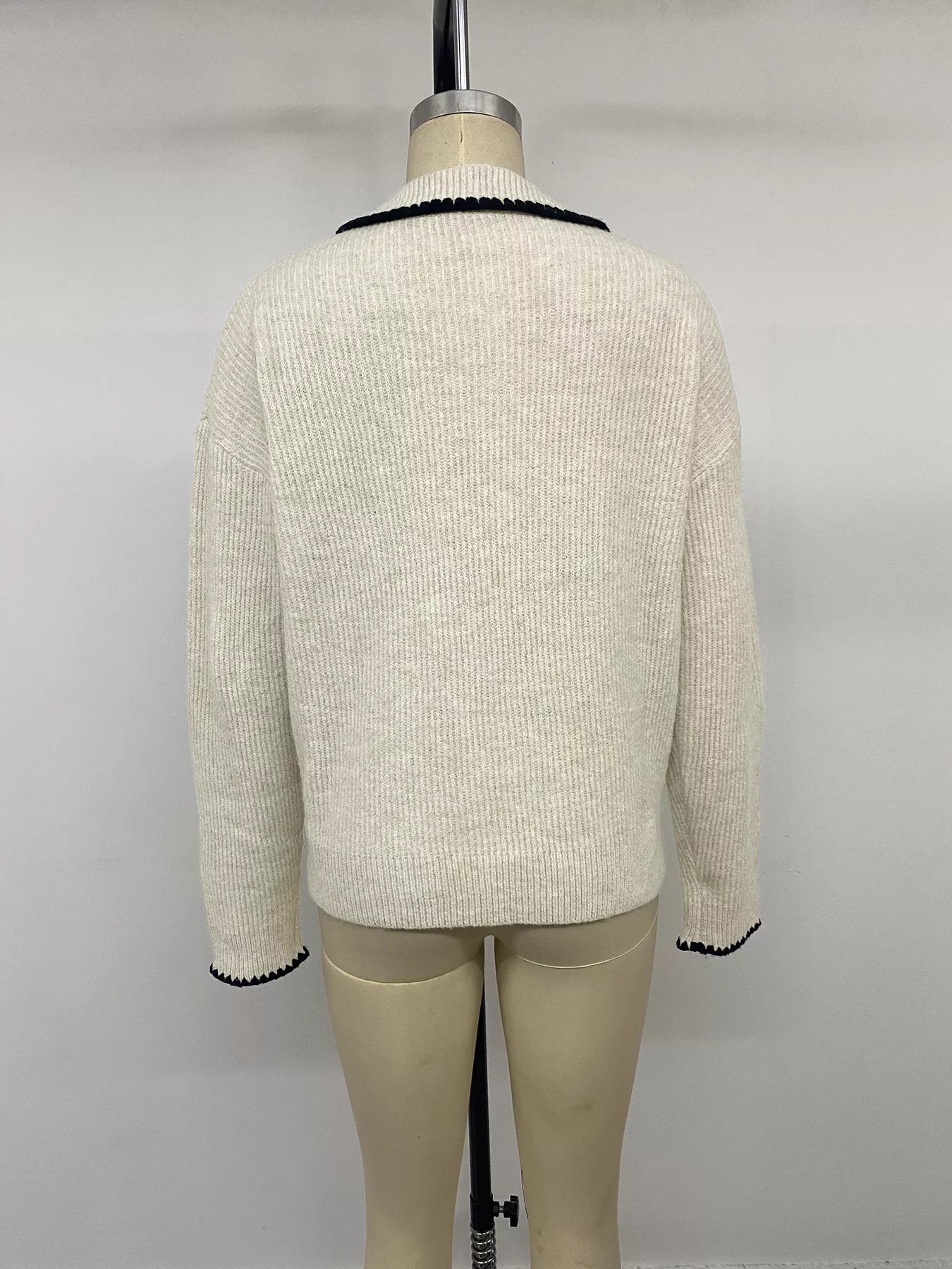 Back view on a mannequin of a plain cream ribbed sweater with black trimmed cuffs