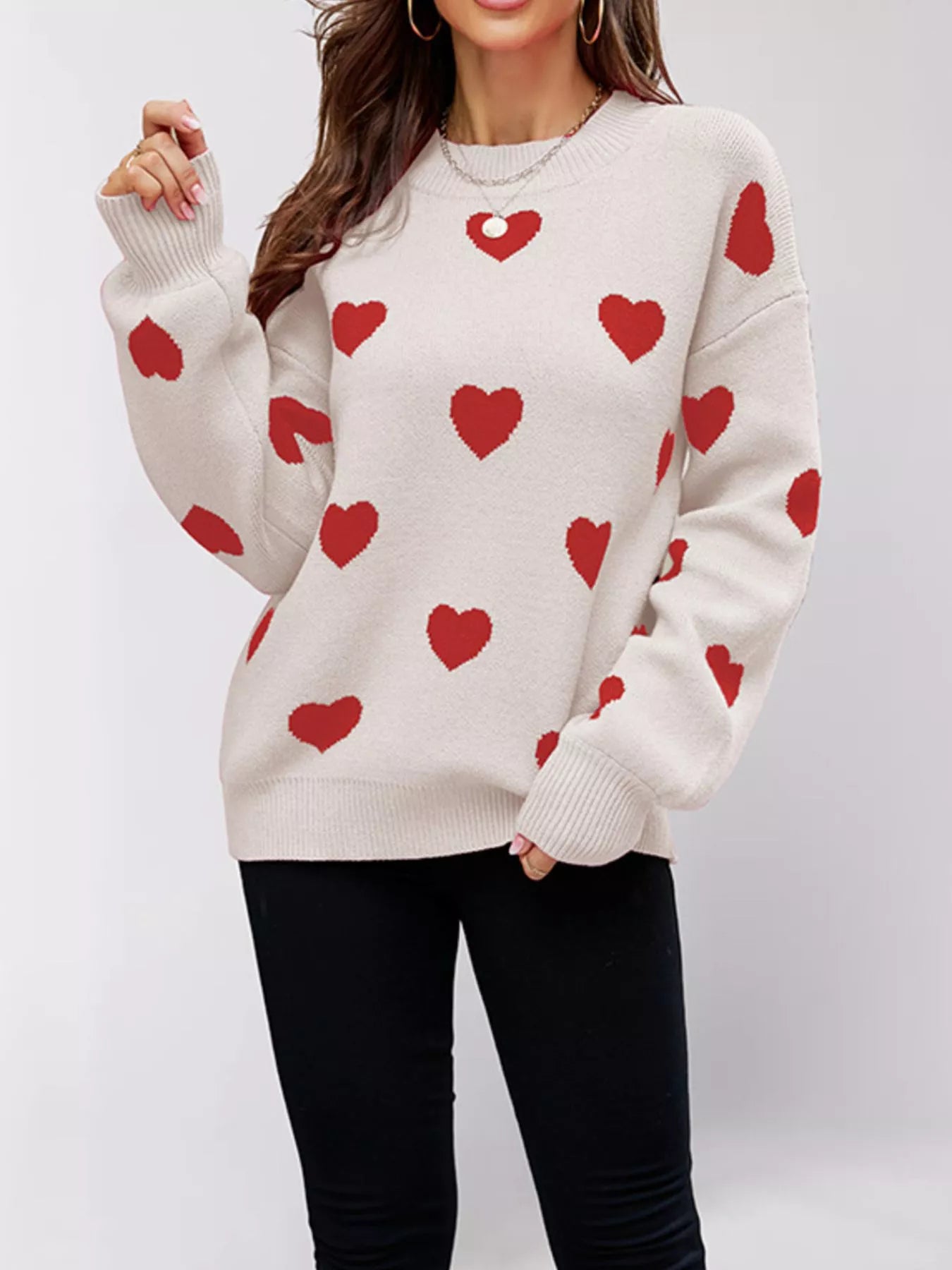 Front view of a cream dropped shoulder sweater with red hearts, one arm raised.