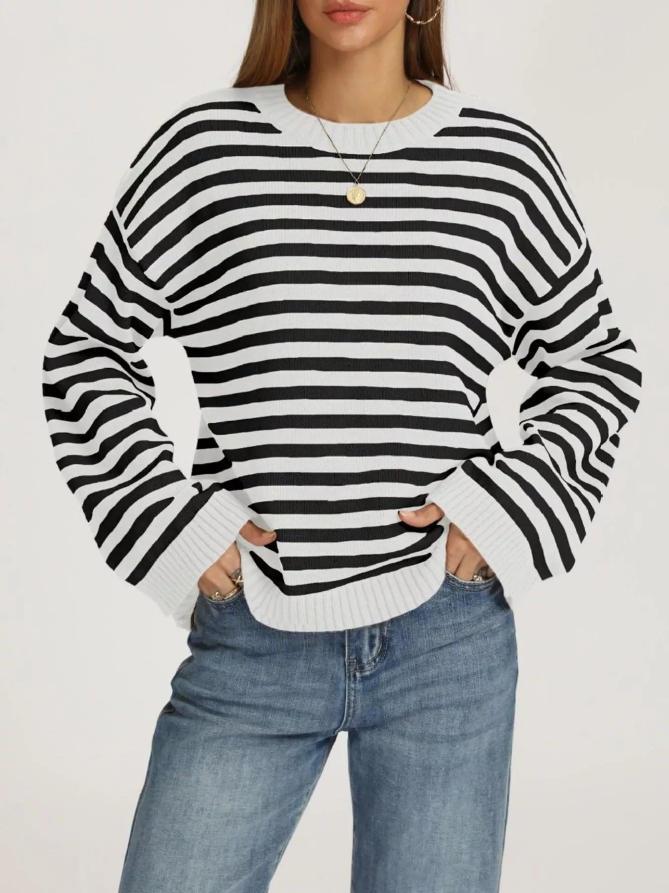 Front view of a white and black striped dropped shoulder sweater with ribbed cuffs worn with jeans.