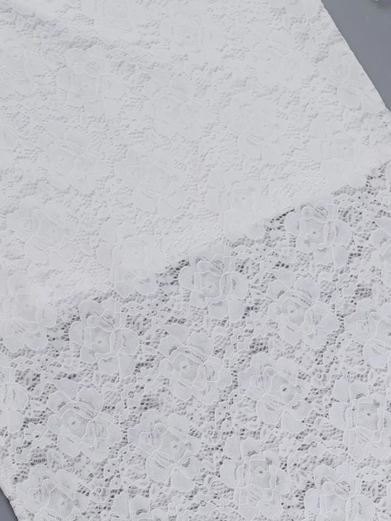 Flat fabric detail of a white lace maxi dress showing the floral lace pattern